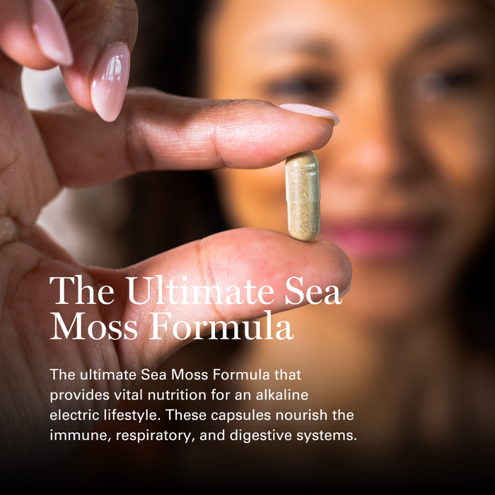 Woman's hand holding a golden Sea Moss capsule with manicured nails against blurred background.