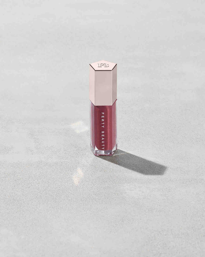 A closed tube of Gloss Bomb Universal Lip Luminizer in the shade RiRi on a grey background.