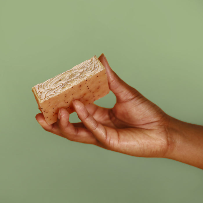 Hand holding Herb'N Eden natural exfoliating lemongrass & patchouli bar soap with botanical swirl top and gentle scrub texture