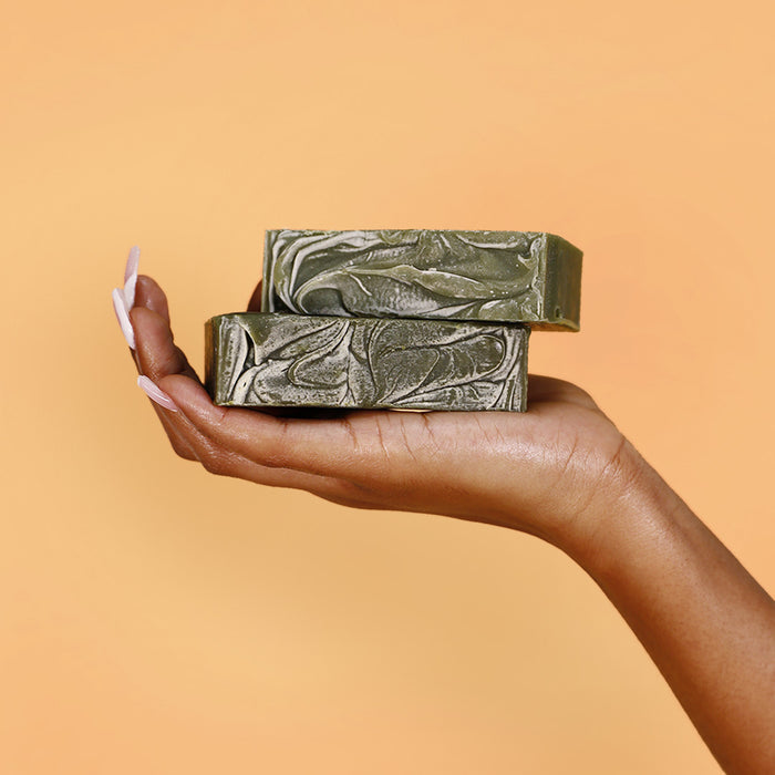 Hand holding stacked Herb'N Eden Neem & Chlorella natural bar soaps with marbled green texture
