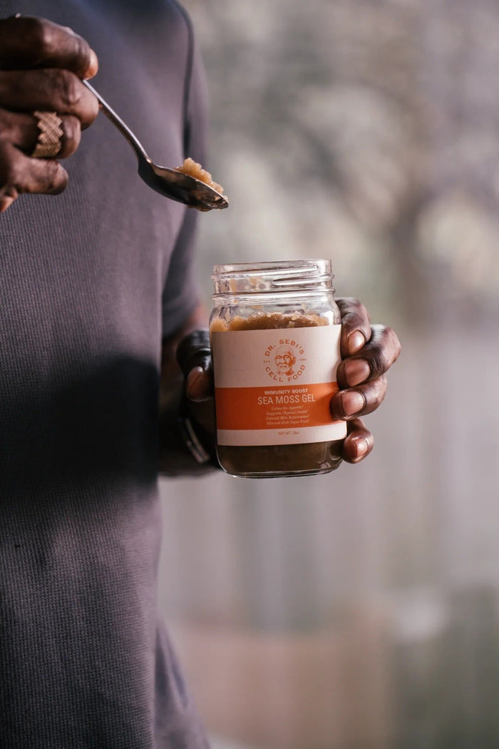 Person holding Dr. Sebi's Sea Moss Gel jar while spooning the product outdoors in natural daylight.
