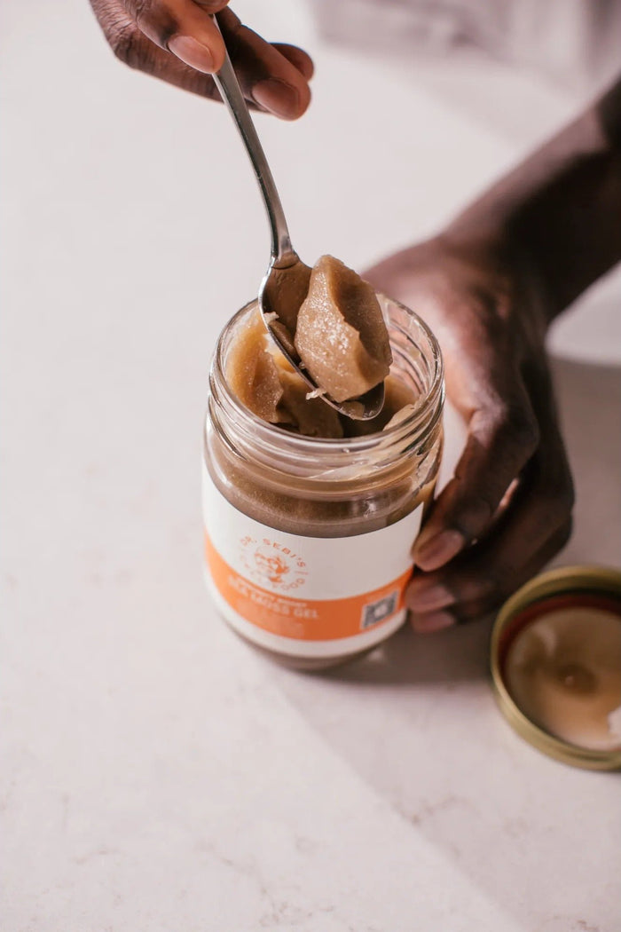 Hand holding spoon of peanut butter from jar with orange label on white surface.