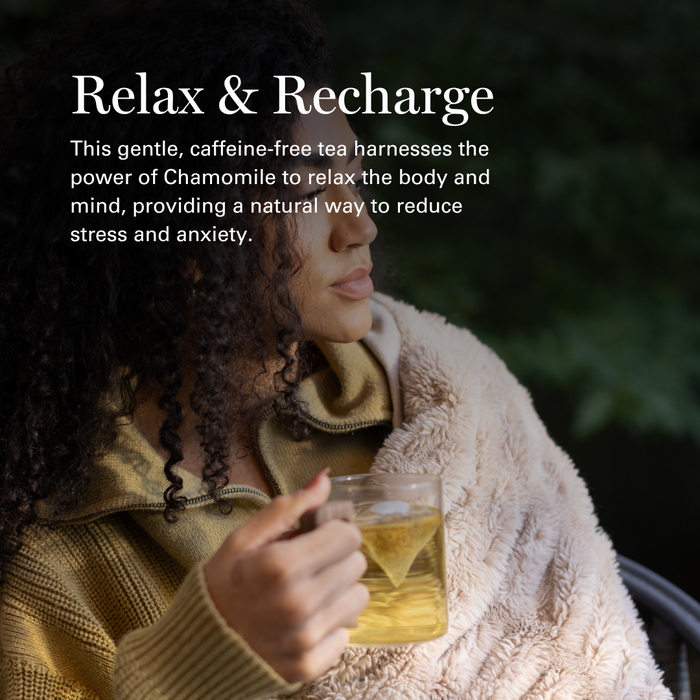 Woman holding chamomile tea in a cozy blanket, relaxing outdoors in natural setting.