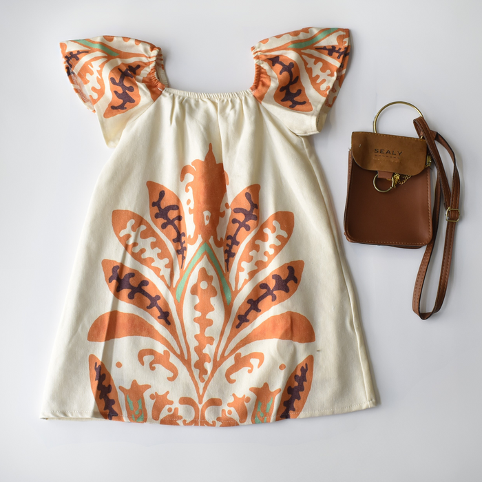 Cream girls’ dress with bold orange and purple floral print and flutter sleeves, paired with a small brown crossbody purse.