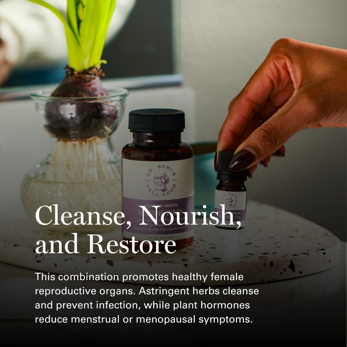 Hand holding Dr. Sebi's Female Health supplement bottles beside a plant on a marble surface with wellness tagline.